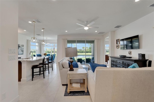 tiled living room featuring ceiling fan with notable chandelier and sink