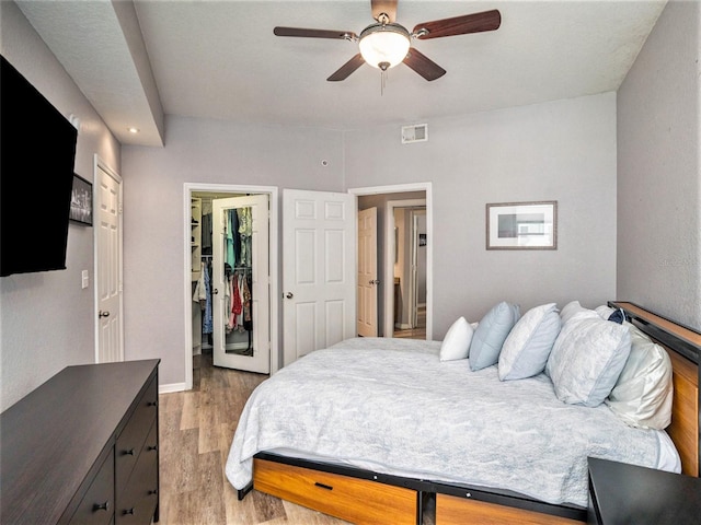 bedroom with a walk in closet, light hardwood / wood-style flooring, a closet, and ceiling fan