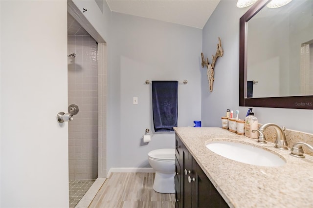 bathroom with hardwood / wood-style floors, a tile shower, vaulted ceiling, toilet, and vanity