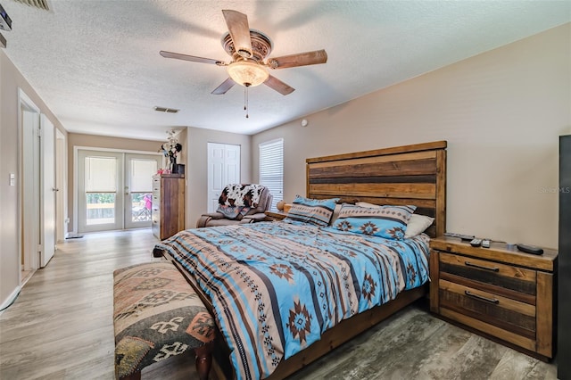 bedroom featuring light hardwood / wood-style flooring, a textured ceiling, french doors, and ceiling fan