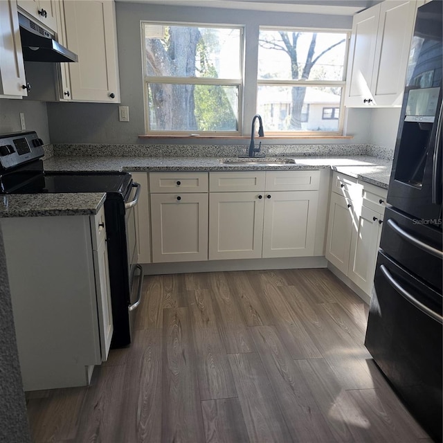 kitchen with black refrigerator, light stone countertops, range with electric cooktop, hardwood / wood-style floors, and white cabinetry