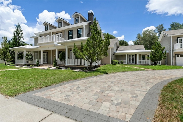 view of front of house featuring covered porch, a garage, a front yard, and a balcony