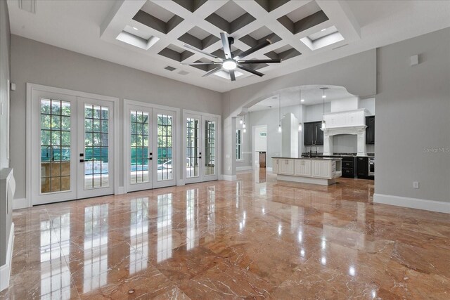 unfurnished living room with coffered ceiling, light tile flooring, beamed ceiling, a high ceiling, and french doors