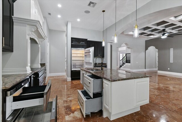 kitchen featuring dark stone counters, coffered ceiling, a center island with sink, ceiling fan, and tile flooring