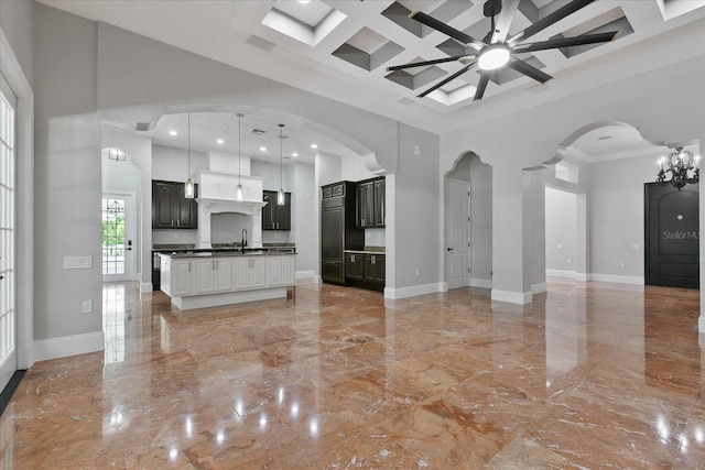 unfurnished living room featuring crown molding, light tile flooring, ceiling fan with notable chandelier, coffered ceiling, and a towering ceiling