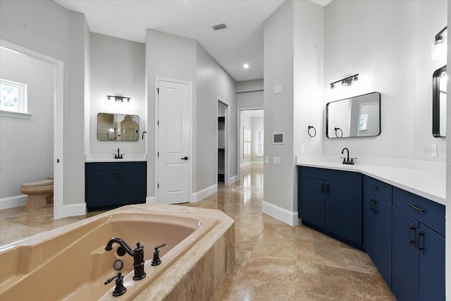 bathroom with tile flooring, tiled tub, dual vanity, and toilet