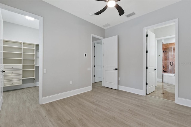 unfurnished bedroom with a walk in closet, a closet, light wood-type flooring, and ceiling fan