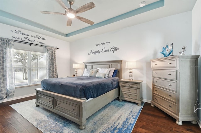 bedroom with dark wood-type flooring, a raised ceiling, and ceiling fan