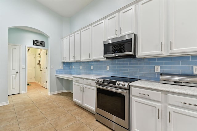 kitchen with tasteful backsplash, light tile patterned flooring, white cabinets, and appliances with stainless steel finishes