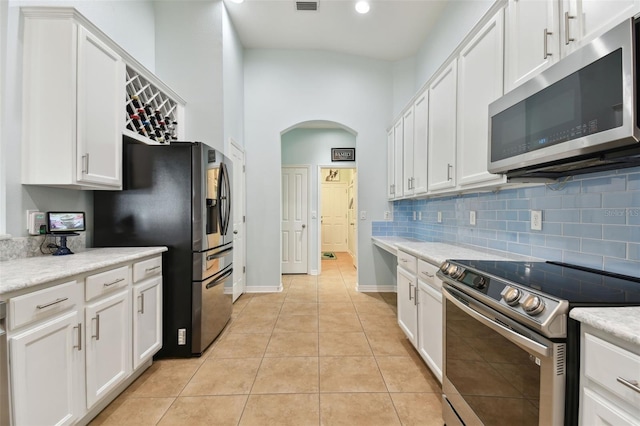 kitchen with light tile patterned floors, decorative backsplash, white cabinets, and appliances with stainless steel finishes