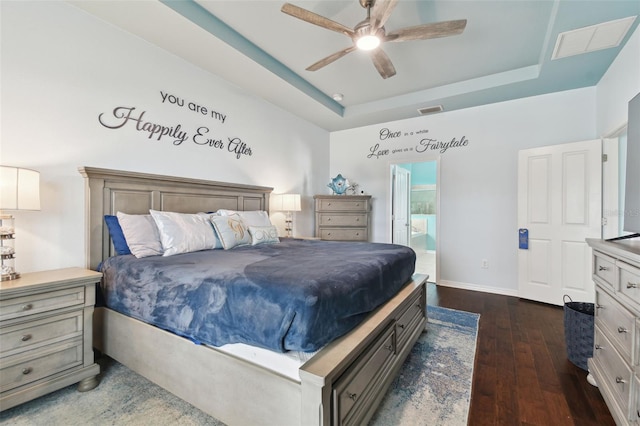 bedroom with dark hardwood / wood-style flooring, connected bathroom, a raised ceiling, and ceiling fan