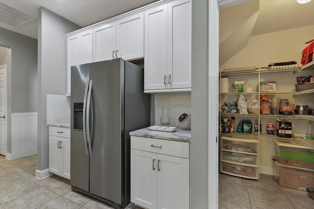 kitchen with white cabinets, stainless steel fridge, light stone counters, and light tile patterned flooring