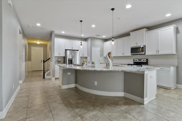 kitchen with white cabinetry, light stone counters, decorative light fixtures, a kitchen island with sink, and appliances with stainless steel finishes