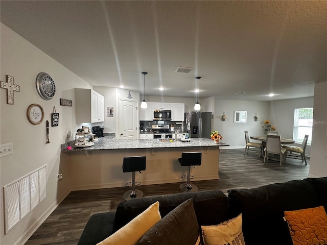 kitchen with stainless steel appliances, white cabinets, dark hardwood / wood-style floors, kitchen peninsula, and a kitchen breakfast bar