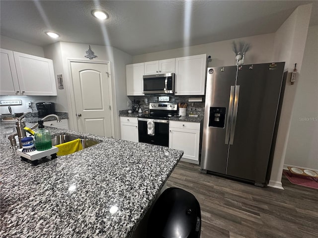 kitchen featuring appliances with stainless steel finishes, white cabinetry, dark stone countertops, and dark hardwood / wood-style floors