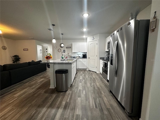 kitchen featuring white cabinetry, stainless steel appliances, hanging light fixtures, dark hardwood / wood-style flooring, and an island with sink