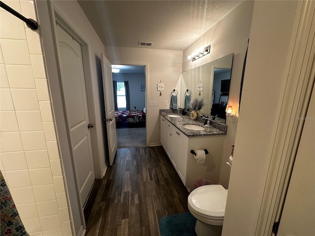 bathroom featuring wood-type flooring, toilet, vanity, and a textured ceiling