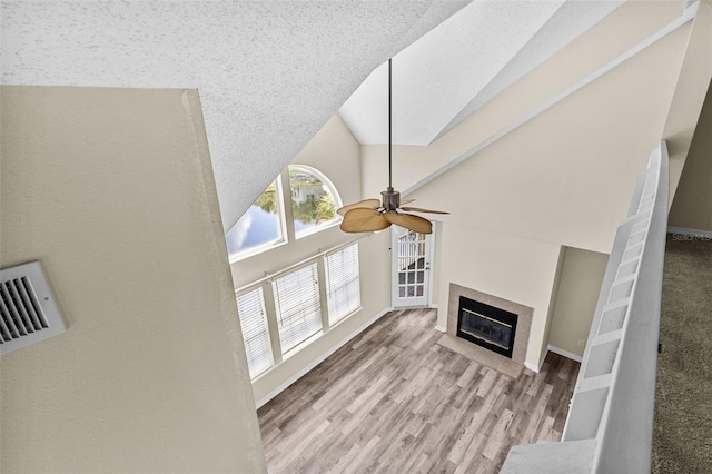 living room with a textured ceiling, ceiling fan, light hardwood / wood-style floors, and high vaulted ceiling