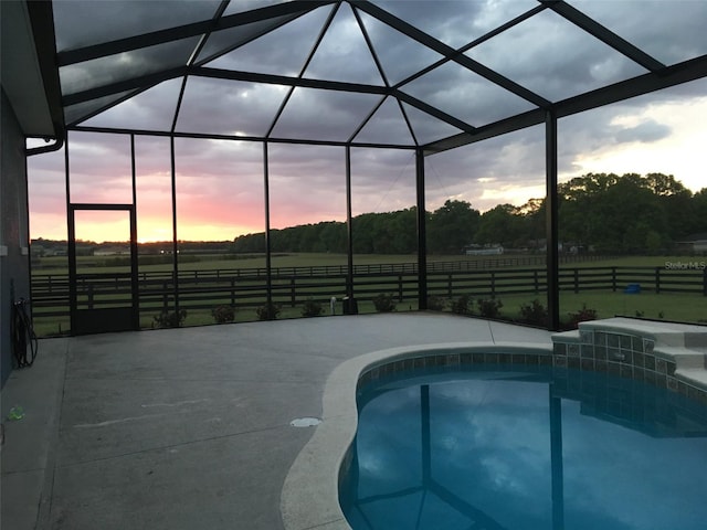 pool at dusk featuring a lanai, a patio, and a rural view