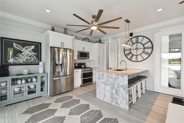 kitchen with stainless steel appliances, sink, decorative light fixtures, white cabinetry, and a breakfast bar area