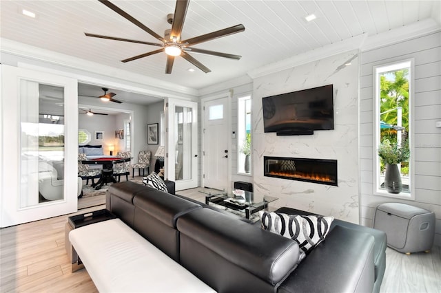 living room with a high end fireplace, ceiling fan, crown molding, light hardwood / wood-style flooring, and wooden ceiling