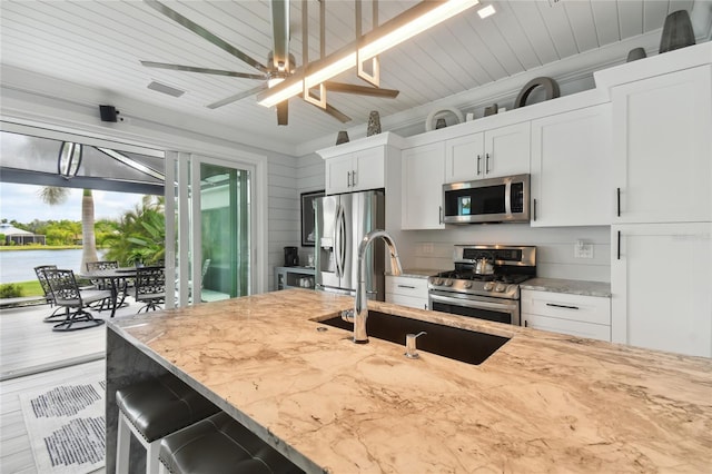 kitchen with light stone countertops, white cabinets, stainless steel appliances, and ceiling fan