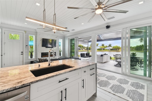 kitchen with light stone countertops, white cabinetry, dishwasher, and sink