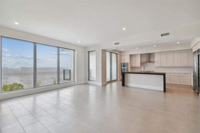 kitchen featuring a kitchen island with sink, a water view, sink, wall chimney exhaust hood, and light tile patterned flooring