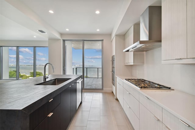 kitchen featuring stainless steel appliances, sink, wall chimney range hood, a large island with sink, and light tile patterned floors