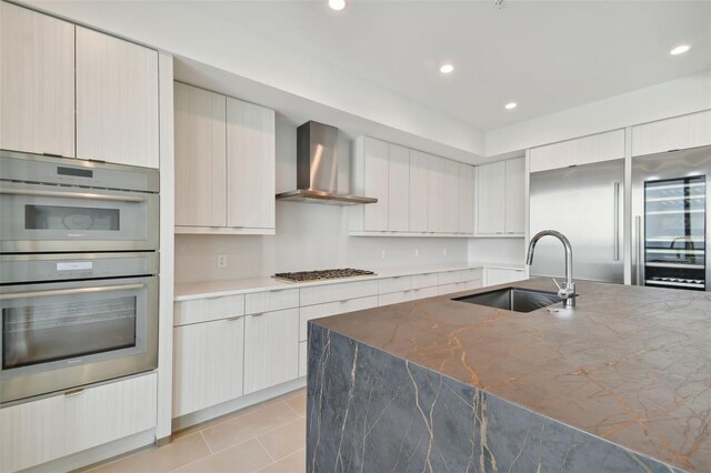 kitchen with dark stone counters, sink, wall chimney exhaust hood, light tile patterned floors, and appliances with stainless steel finishes