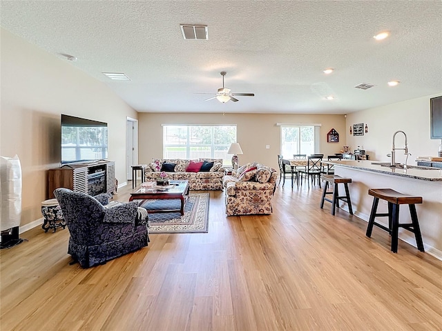 living room featuring ceiling fan, sink, light hardwood / wood-style floors, and a textured ceiling