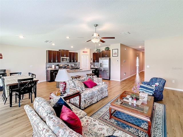 living room with ceiling fan, a textured ceiling, and light hardwood / wood-style flooring