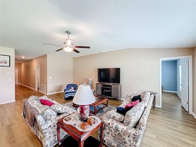 living room featuring ceiling fan, light hardwood / wood-style floors, lofted ceiling, and a textured ceiling