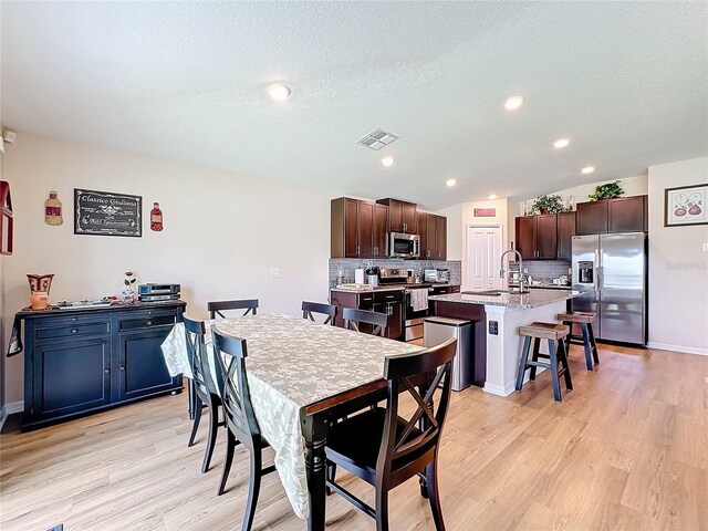 dining space with a textured ceiling, sink, and light hardwood / wood-style flooring