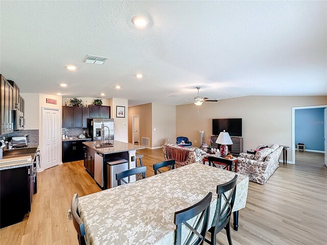 dining room featuring ceiling fan, sink, a textured ceiling, and light wood-type flooring