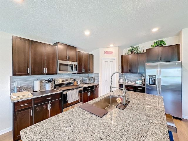 kitchen featuring sink, decorative backsplash, a textured ceiling, light stone counters, and stainless steel appliances