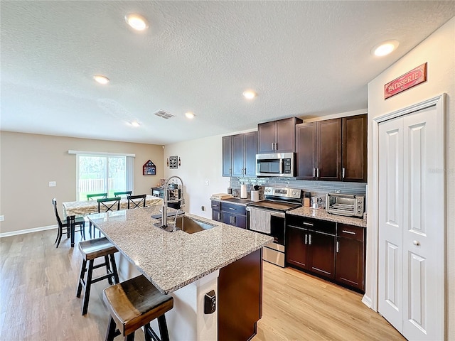 kitchen featuring a kitchen island with sink, sink, appliances with stainless steel finishes, light hardwood / wood-style floors, and a breakfast bar area