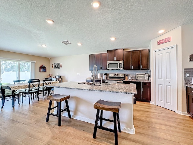 kitchen featuring a breakfast bar area, decorative backsplash, a kitchen island with sink, and stainless steel appliances