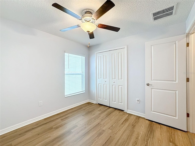 unfurnished bedroom with a textured ceiling, a closet, light hardwood / wood-style floors, and ceiling fan