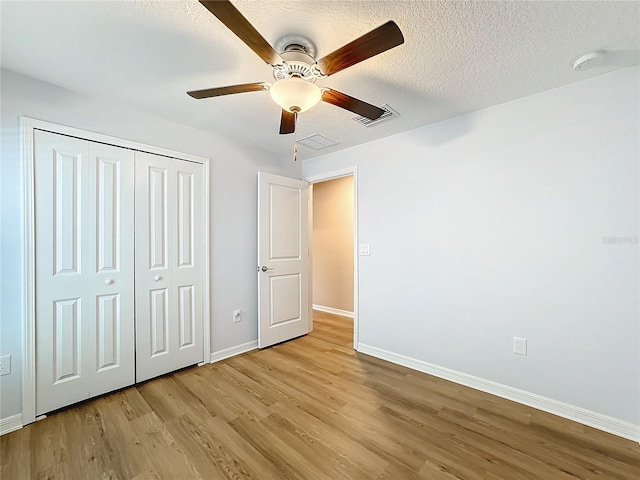 unfurnished bedroom with ceiling fan, light wood-type flooring, a textured ceiling, and a closet