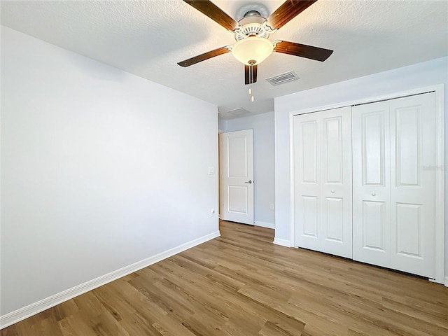 unfurnished bedroom with ceiling fan, a closet, a textured ceiling, and light hardwood / wood-style flooring