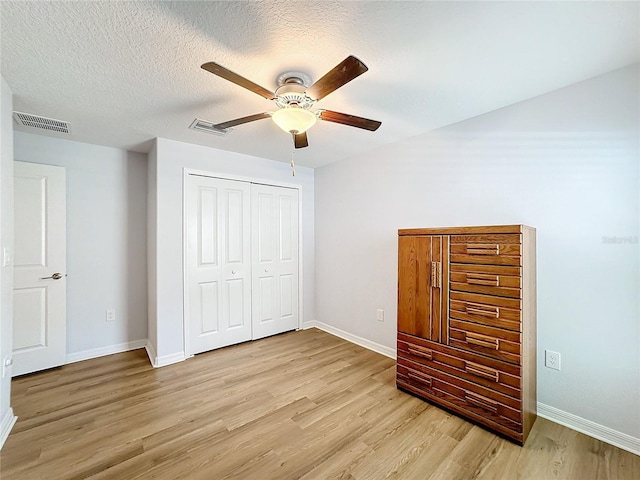 unfurnished bedroom with ceiling fan, light hardwood / wood-style floors, a textured ceiling, and a closet