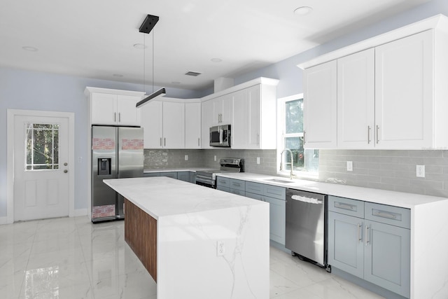 kitchen featuring a kitchen island, appliances with stainless steel finishes, white cabinetry, sink, and hanging light fixtures