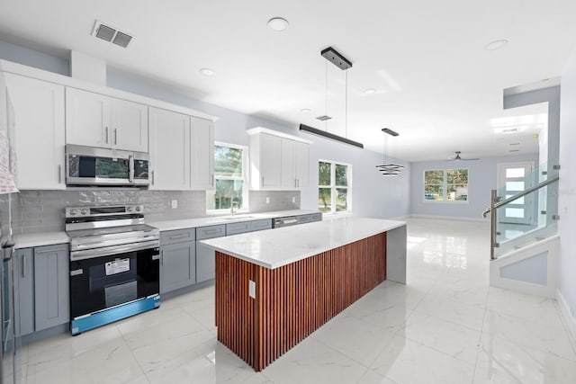 kitchen with appliances with stainless steel finishes, white cabinetry, gray cabinetry, hanging light fixtures, and a center island