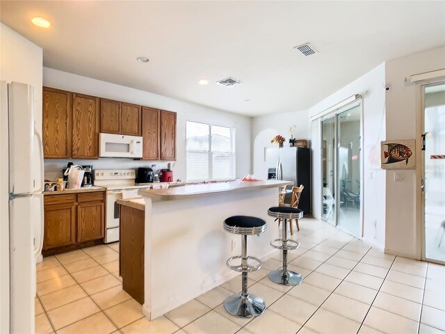 kitchen with light tile patterned floors, white appliances, a kitchen island, and a kitchen bar