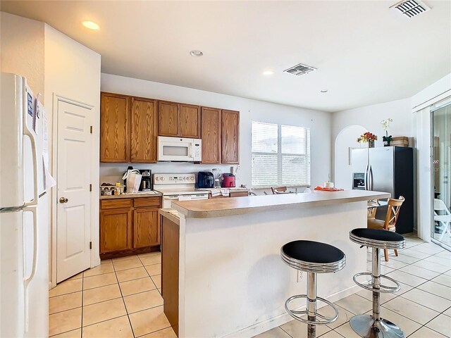 kitchen with light tile patterned flooring, a kitchen island, white appliances, and a breakfast bar