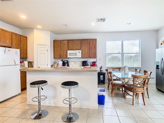 kitchen with kitchen peninsula, white appliances, light tile patterned floors, and a breakfast bar