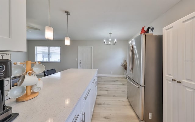 kitchen featuring stainless steel fridge, light stone countertops, white cabinetry, and hanging light fixtures