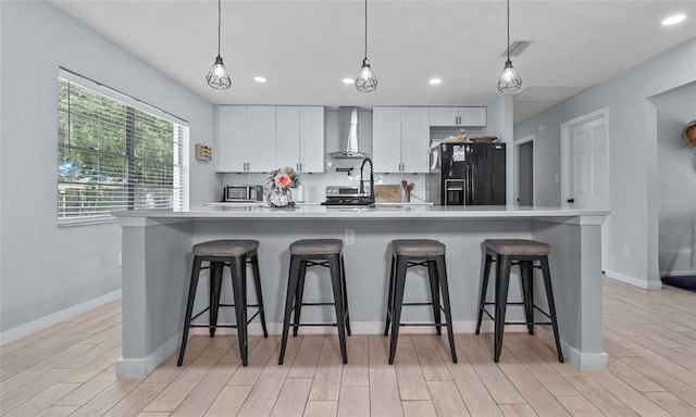 kitchen with hanging light fixtures, white cabinetry, wall chimney exhaust hood, a large island, and black fridge