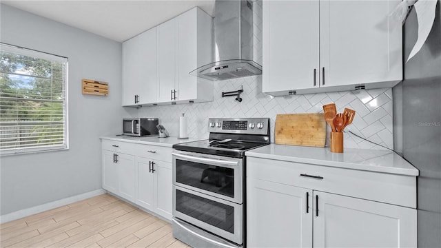 kitchen featuring wall chimney exhaust hood, white cabinetry, and appliances with stainless steel finishes